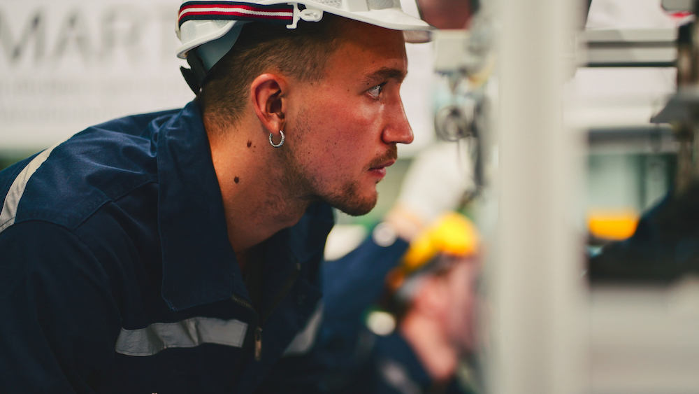 engineer in white hardhat crouched down inspecting something