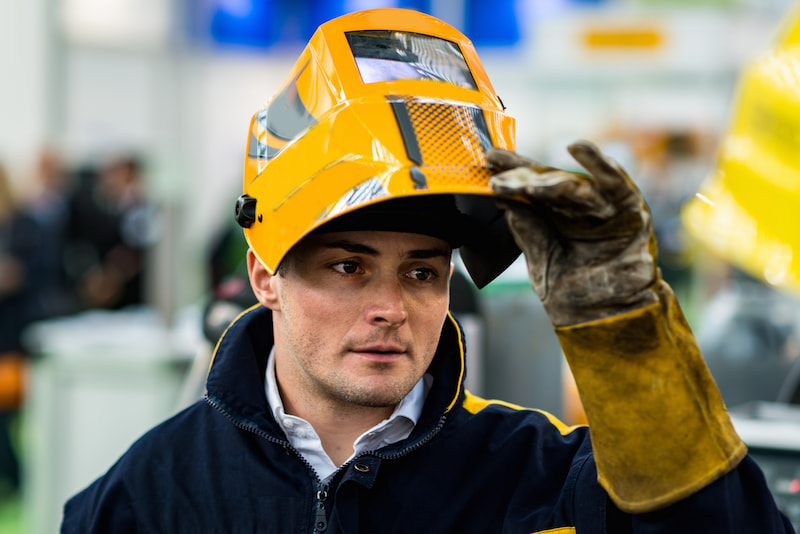 man lifting his yellow hardhat wearing safety gloves